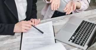 Mains tenant un contrat d'assurance ouvert à côté d'une valise et d'une liste de vérification