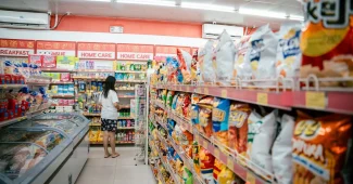 Gros plan sur une étagère de supermarché avec des produits d'apéritif estivaux et une main de client lisant les étiquett