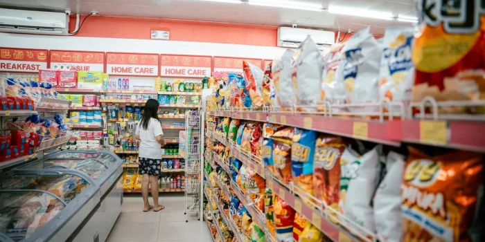 Gros plan sur une étagère de supermarché avec des produits d'apéritif estivaux et une main de client lisant les étiquett