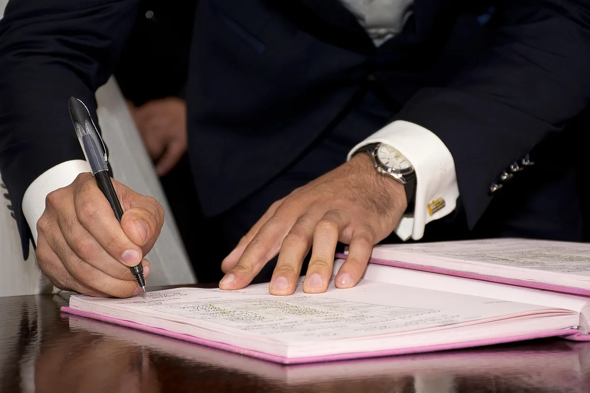 Deux personnes anonymes signant des documents chez le notaire en plein jour